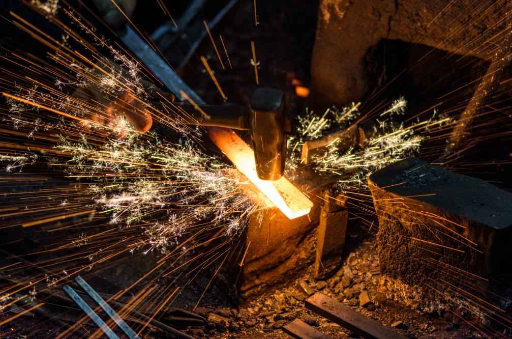 Blacksmith forging the molten metal on the anvil with spark fireworks