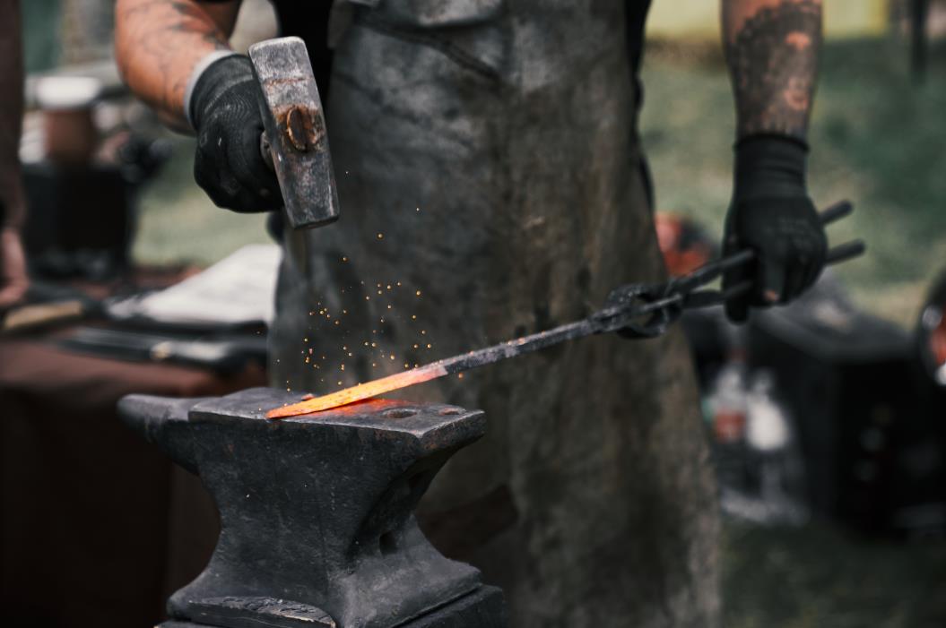 Blacksmith manually forging molten metal on anvil.