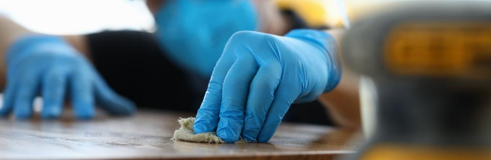 Carpenter in gloves cleans polishes wooden surface