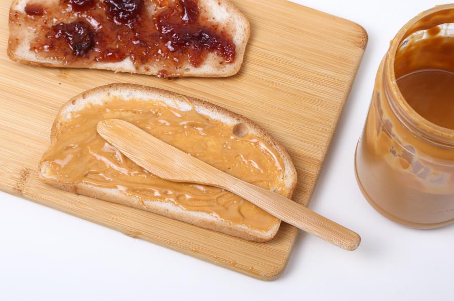 Bamboo cutting baord serving bread smeared with peanut butter and jelly