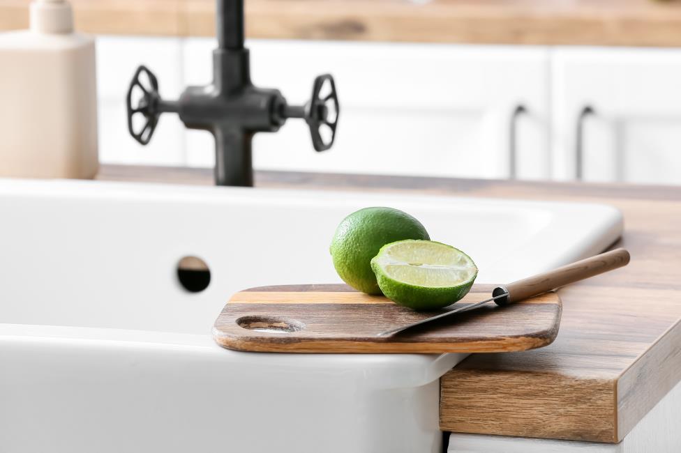 Cutting board with lime and knife on ceramic sink in kitchen, closeup