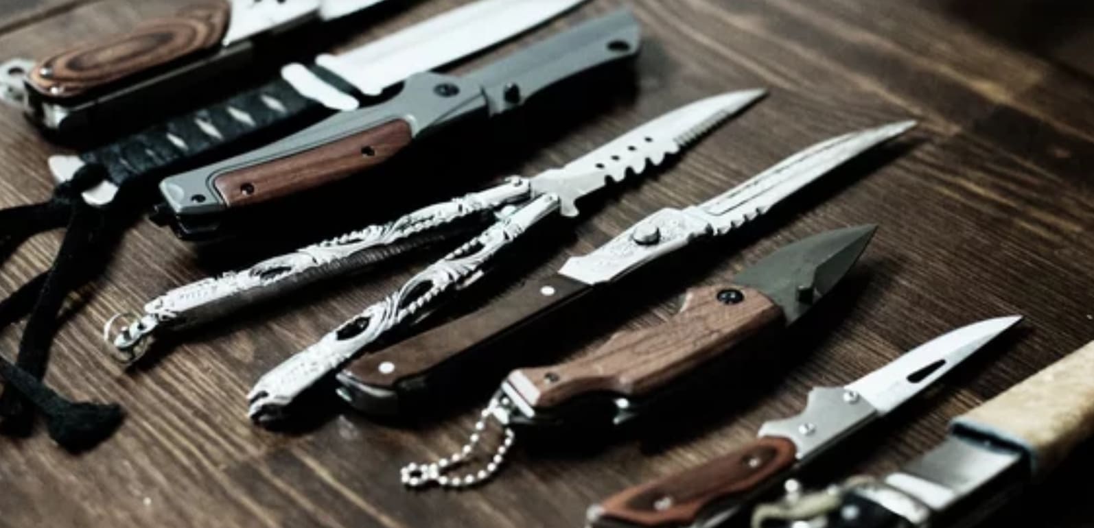 A series of pocket knives put side by side on a wooden table