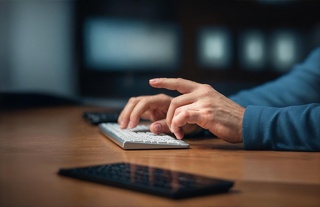 A man is using his computer and phone to contact others.