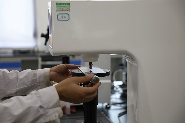 Technician positioning a blade on a Rockwell hardness tester at LeeKnives